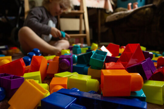 Colorful plastic constructor blocks on foreground with blurred toddler playing at home