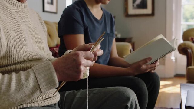Picking needles, senior in cream knit forming stitches on home couch, teen using notebook to learn