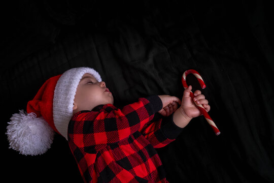 Sleeping baby in santa hat holding candy cane.