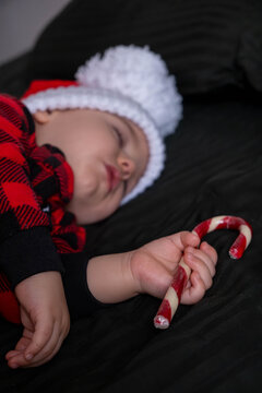 Sleeping baby in santa hat holding candy cane.