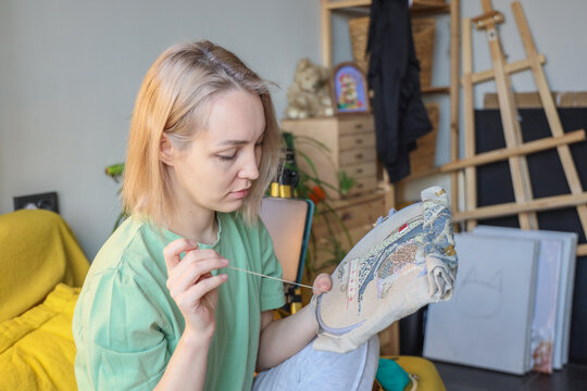 Young Woman Carefully Embroidering Detailed Fabric Hoop In Cozy Home Studio, Surrounded By Creative Tools, Easel, Storage Boxes, And Soft Daylight, Showing Focused Handmade Textile Art