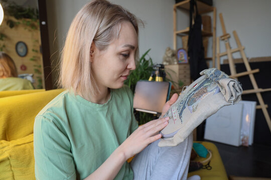 Blonde Woman In Mint Shirt Carefully Embroidering Detailed Fabric Art While Sitting In Cozy Home Studio, Showing Focused Concentration, Handmade Craft Process, Soft Natural Light