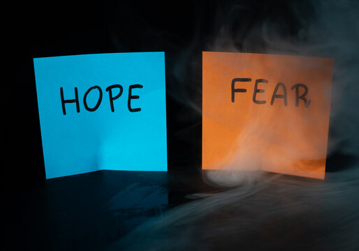 Blue sticky note HOPE and orange sticky note FEAR with dramatic swirling smoke on dark background. Concept of emotional contrast, mental health and inner conflict.