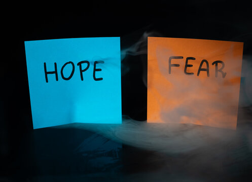 Blue sticky note HOPE and orange sticky note FEAR with dramatic swirling smoke on dark background. Concept of emotional contrast, mental health and inner conflict.
