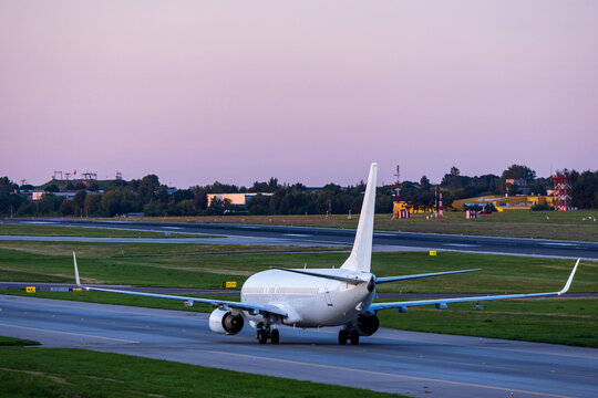 View of a white passenger airplane taxiing on the runway at Vilnius International Airport during golden hour, with airport infrastructure in the background, Vilnius, Vilniaus apskritis, Lithuania.