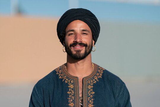 Smiling bearded man in embroidered tunic and dark turban portrait for cultural lifestyle background and male fashion headshot usage