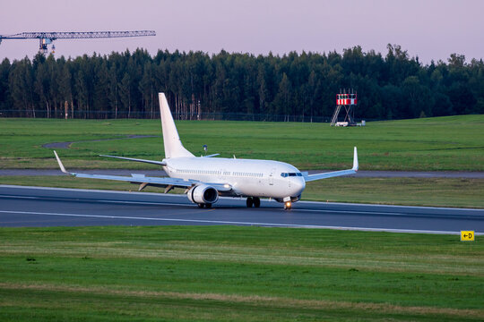 View of a white passenger airplane taxiing on the runway at Vilnius International Airport with green grass and trees in the background in Vilnius, Vilniaus apskritis, Lithuania.