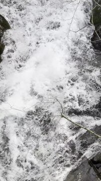 Vertical shot of white foam and bubbles in a rushing waterfall.