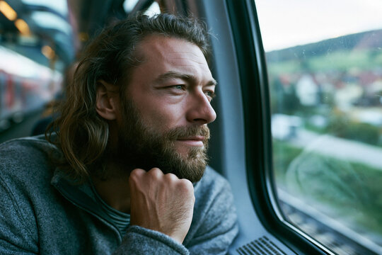 Thoughtful Bearded Man Looking Through Train Window While Traveling