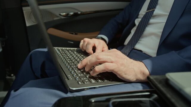 Cropped shot of hands of unrecognizable businessman typing on laptop keyboard while sitting in backseat of luxury car. Ideal for corporate communications, remote work, and executive travel concepts