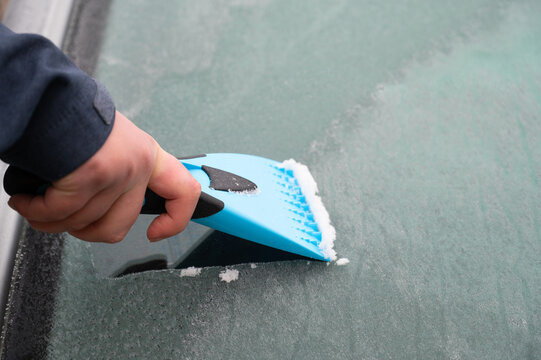 Driver is removing snow from car windshield with ice scraper and broom, clean car window from icy frost, winter season