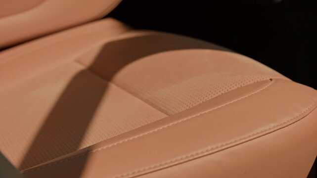 Beige leather car seat showing detailed stitching and perforated texture under shifting sunlight. Perfect for luxury automotive marketing, car detailing promos, or vehicle interior design showcases