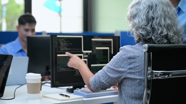 Senior Asian female software engineer coding on a desktop computer while a team member manages project tasks on an agile scrum board