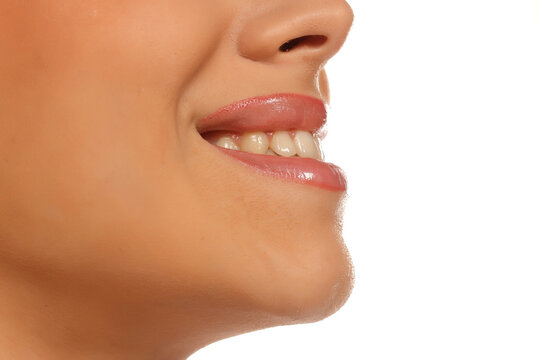 Extreme close-up of woman's smiling mouth, teeth visible, glossy lips, profile view, on white background