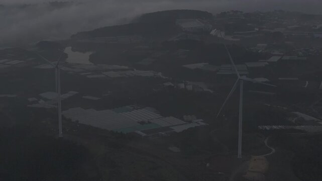 Aerial drone view of Cau Dat tea hills and wind turbines at sunset in Xuan Truong, Da Lat, Lam Dong, Vietnam, showcasing renewable energy and scenic highland landscapes.