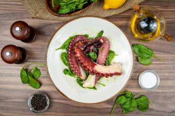 Grilled octopus served on fresh spinach with creamy potato puree, food flat lay, top-view on a rustic wooden table © Microgen