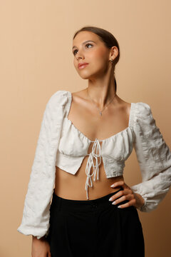 Studio shot of a woman looking up and away, wearing a white puff sleeve crop top, on beige background