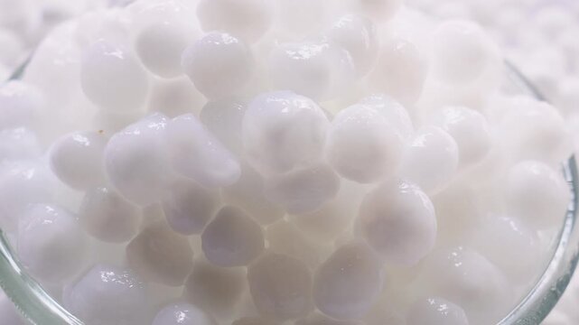 Side view shot of Sabudana kheer in a glass bowl along with some raw tapioca pearls sago spread on the background.