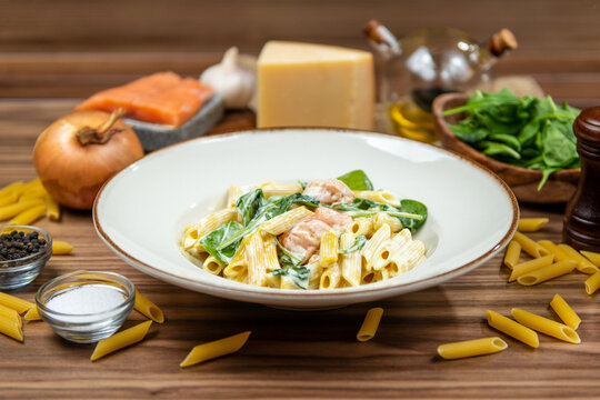 Creamy salmon penne pasta with spinach and parmesan cheese, restaurant main course, side view on a rustic wooden table
