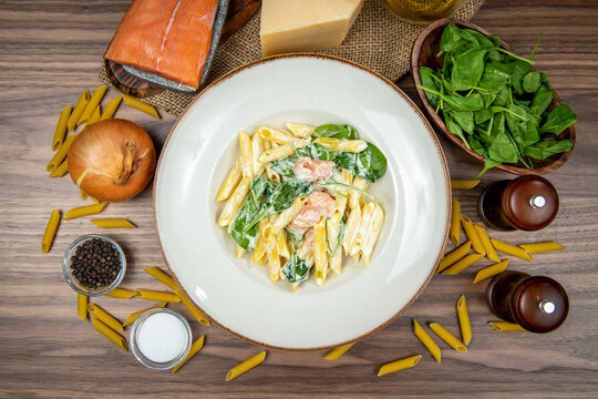 Salmon penne pasta with spinach and parmesan cheese, food flat lay, top-view on a rustic wooden table