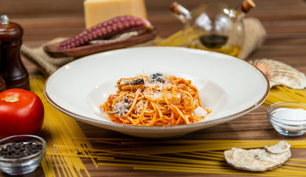 Spaghetti with octopus in tomato sauce topped with parmesan cheese, restaurant seafood pasta, side view on a rustic wooden table