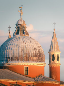 View of the dome and bell tower of San Giorgio Maggiore church illuminated by warm golden hour light in Venice, Veneto, Italy.