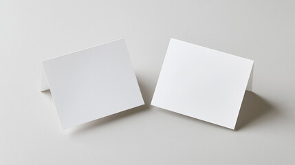 Fototapeta premium A clean 3D render mockup of two folded blank white cards or place cards on a neutral light grey background, ideal for stationery branding presentations.