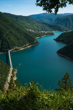 View of Piva Lake with its turquoise water, a long bridge crossing the narrow section, surrounded by lush green mountains and dense forests in Pluzine Municipality, Montenegro.