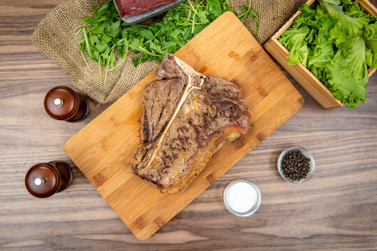 Grilled T-bone steak served on a wooden board, food flat lay, top-view on a rustic wooden table