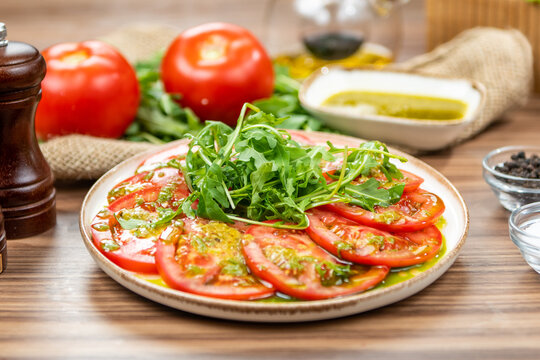 Fresh tomato carpaccio with arugula and herb dressing, restaurant appetizer, side view on a rustic wooden table