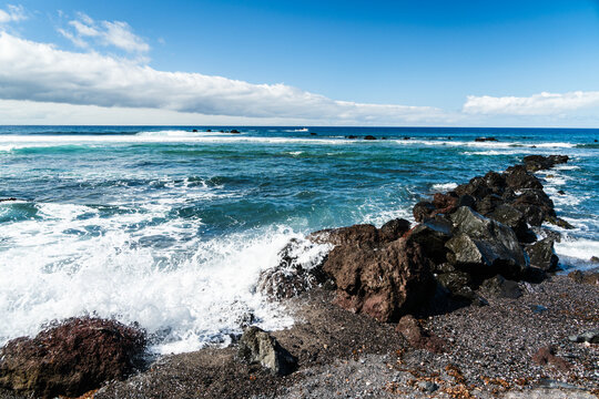View of waves crashing against dark volcanic rocks along the coastline in Las Galletas, Canary Islands, Spain.