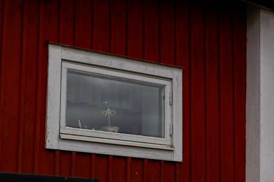 View of a traditional red wooden wall with a white-framed window displaying a small Swedish flag and decorative items in Gammelstaden, Norrbotten County, Sweden.