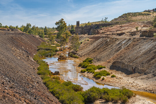 View of the historic Minas de Sao Domingos mining site featuring a stream with mineral-rich water flowing through rocky banks and sparse vegetation in Corte do Pinto, Beja District, Portugal.