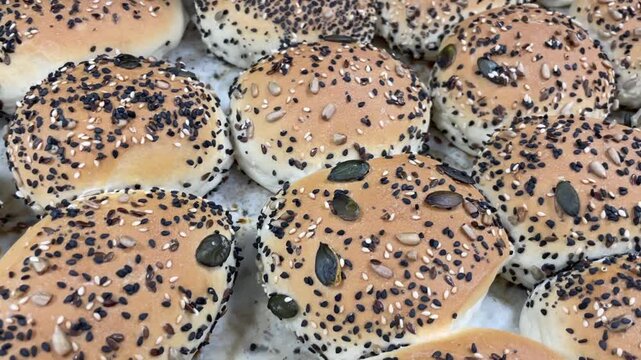 multiple seeded dinner rolls sit tightly arranged on baking tray, showing golden browning, textured crusts, mixed seeds, and rounded tops in warm light with fine
