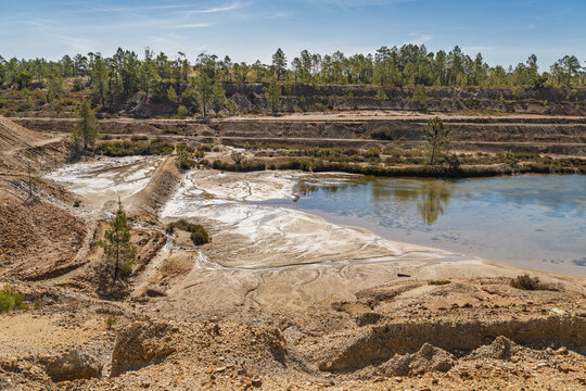 View of Minas de Sao Domingos featuring the abandoned open-pit mine landscape with mineral-rich water, reddish soil, and pine forest in Corte do Pinto, Beja District, Portugal.