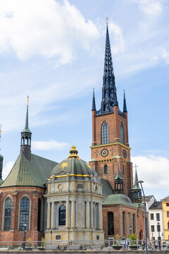 View of Riddarholmen Church with its distinctive cast-iron spire, brick facade, and ornate dome under a blue sky in Stockholm, Stockholm County, Sweden.