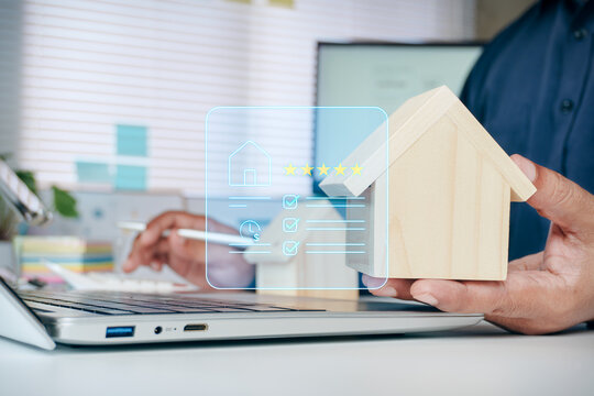 Hand holding wooden house model with digital real estate checklist and five-star rating hologram icons, concept of property valuation, home buying investment, mortgage loan, and housing review.