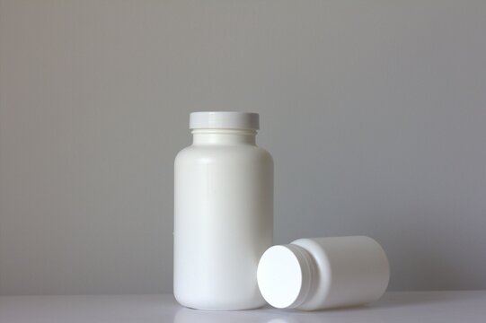 Large blank white plastic medicine bottle standing on a clean white background with a matching smaller bottle lying beside it