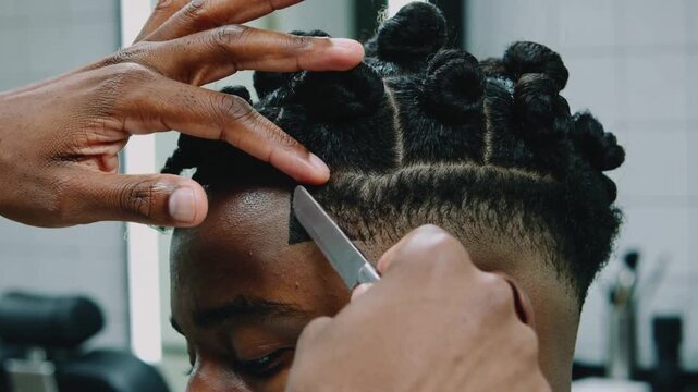 Lifting hair, barber guiding straight razor in barbershop, defining hairline, keeping twisted buns