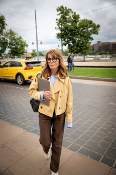 Smiling blond haired woman with laptop walking in the city
