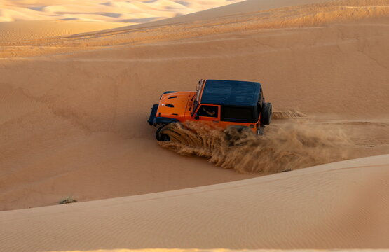Al Dhafra Region, Abu Dhabi, United Arab Emirates - 16 November 2018: View of an orange off-road vehicle driving through the sand dunes of the Liwa desert, kicking up sand.