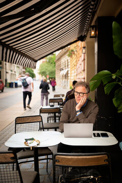Confident senior businessman sitting at a table and using his laptop at an outdoor caf&eacute;