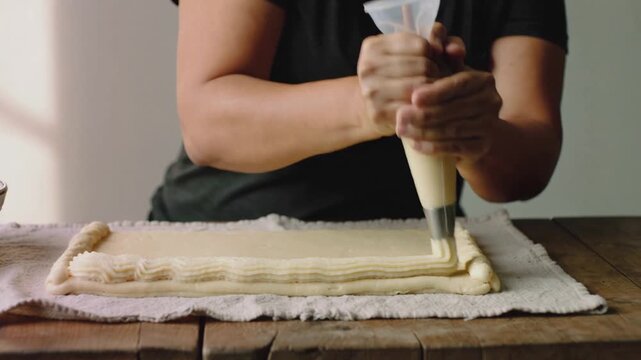 Squeezing bag, woman in V-neck guiding star tip clockwise on pastry, piping ridged edge, bowl left