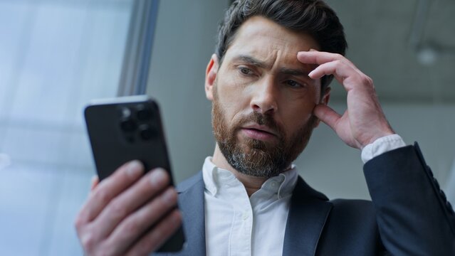 Upset Caucasian middle-aged business man receive bad notification with mobile phone in office. Stressed 40s businessman male executive feeling frustration with smartphone loosing connection problem