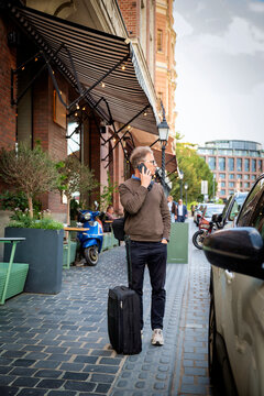 Senior man with suitcase using smartphone on city street