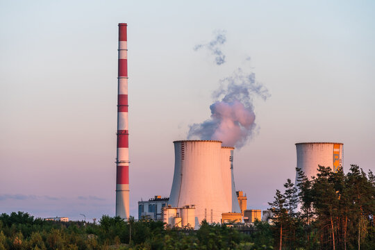 Jaworzno, Poland - 23 August 2026: View of Jaworzno Power Station with its tall red and white striped chimney and cooling towers emitting steam against a soft sunset sky.