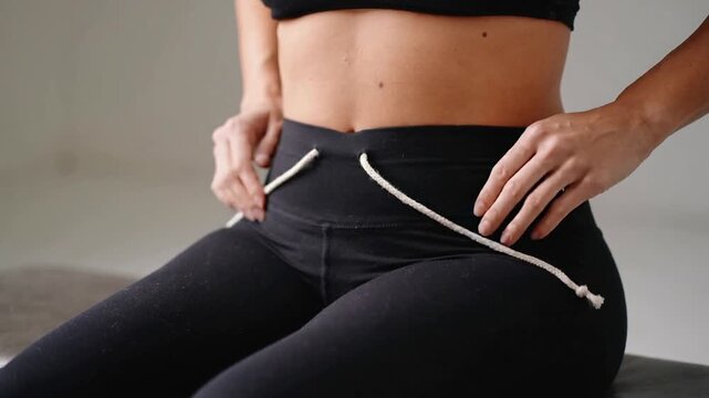 Holding cream braided cord, fit woman threading through high-waist leggings to adjust fit in studio