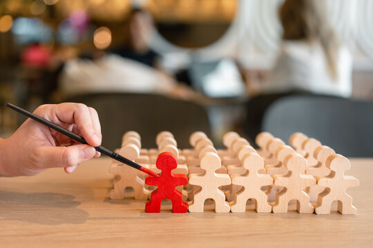 Talent recruitment and leadership concept with hand painting wooden figure in red among crowd on table for employee selection, career training, standout candidate and business development.