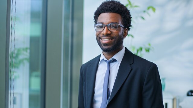 Close up joyful cheerful African American business man smiling looking at camera businessman male guy professional near window agent smile posing working in workplace office enjoying work ambition