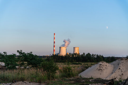 Jaworzno, Silesian Voivodeship, Poland - 23 August 2026: View of the Jaworzno power plant with cooling towers and a tall chimney emitting smoke, set against a clear sky with a visible moon.